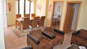A dining area with a table and chairs, a sofa with armrests, and a door leading to another room. - Casa Biontica (Cómpeta)