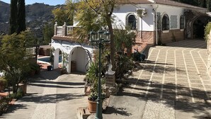 A white building with a tiled roof, a covered patio, and a view of a hilly landscape. - Casa Biontica (Cómpeta)