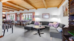 A cozy living room with a wooden ceiling, a round coffee table with candles, a grey sofa, and a dining area with striped chairs. - Lovely home in Mariager with WiFi (Mariager)