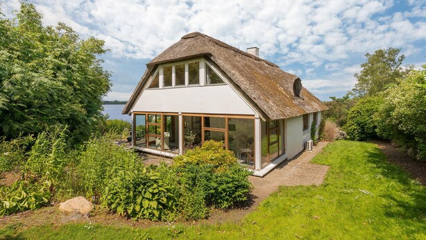 A house with a thatched roof, large windows, and a view of a lake. - Lovely home in Mariager with WiFi (Mariager)