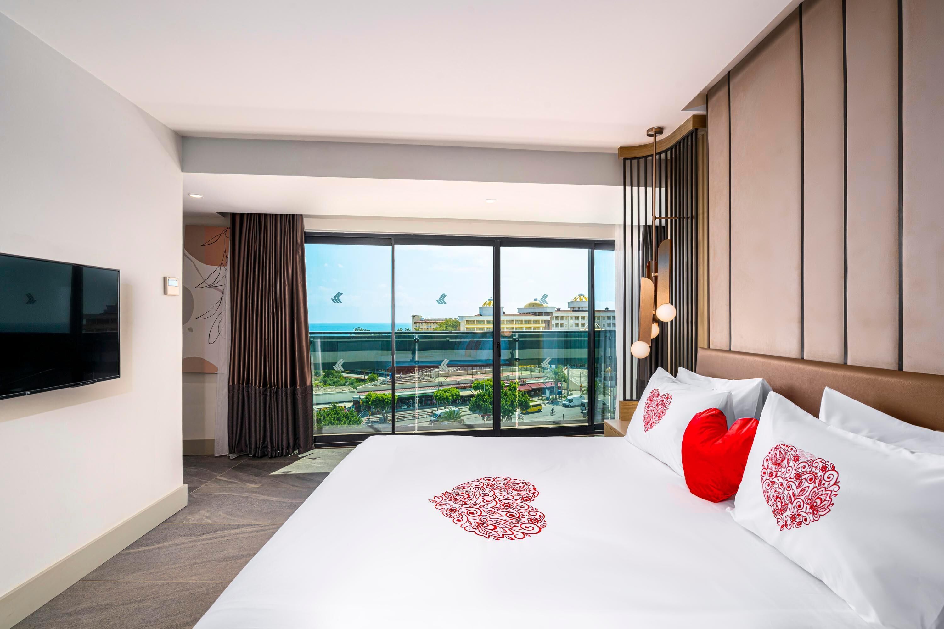 A hotel room with a large bed, a flat-screen TV, and a balcony with a city view.