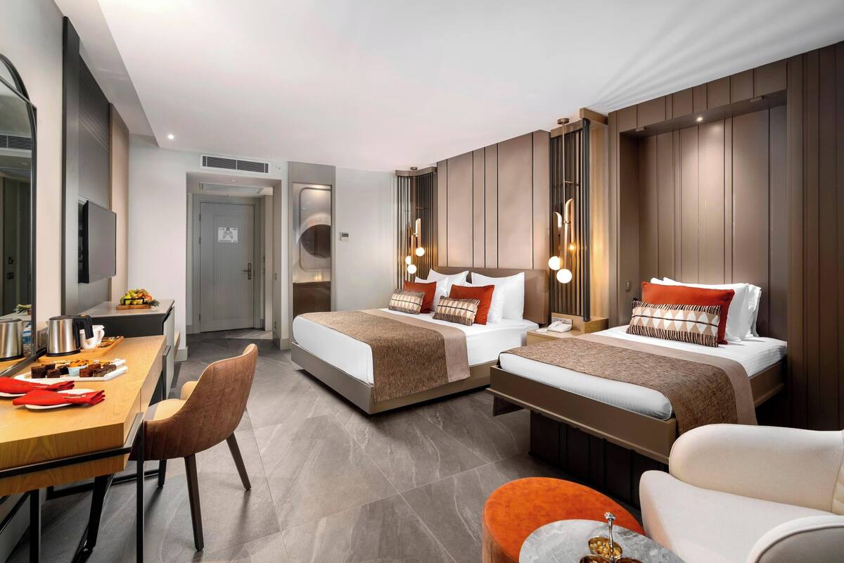 A hotel room with two beds, a desk with a chair, and a dining table with chairs.