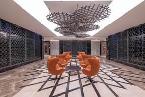 A modern lobby with geometric patterned walls, a central seating area with orange chairs, and a unique ceiling design. - Calyptus Kirman Premium - Ultra All Inclusive (Manavgat)