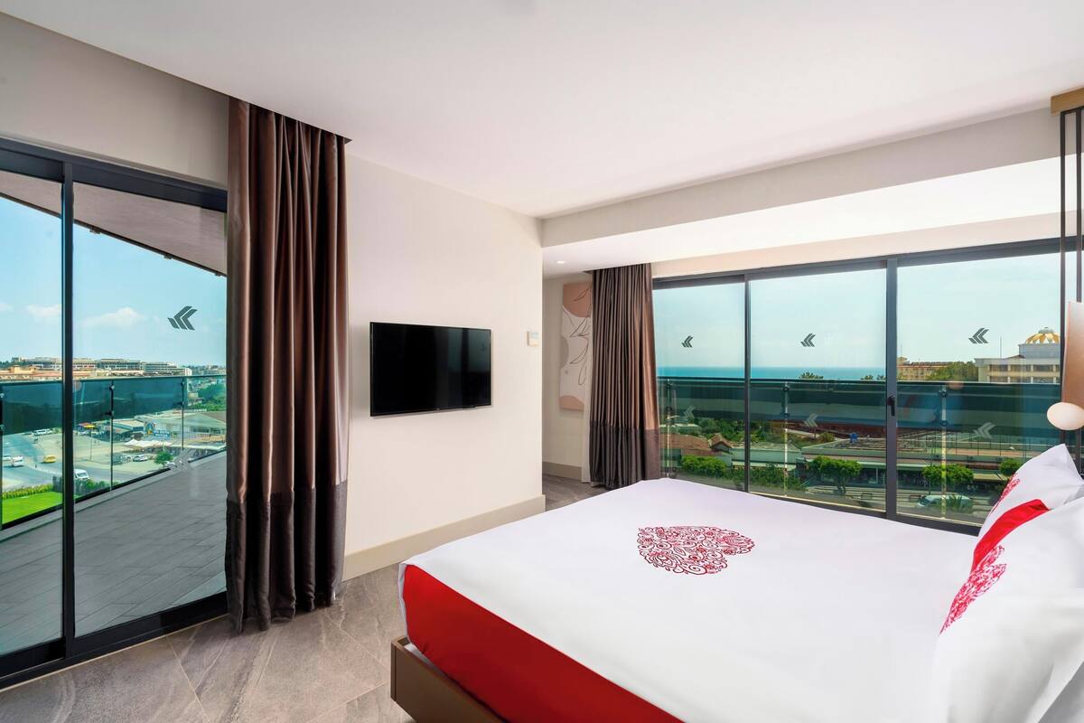 A hotel room with a large bed, a flat-screen TV, and a balcony with a city view.
