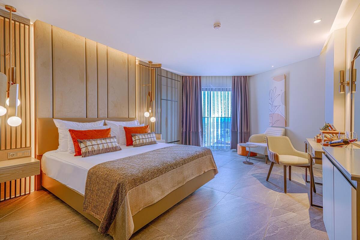 A modern hotel room with a large bed, a desk, and a view of the outdoors.