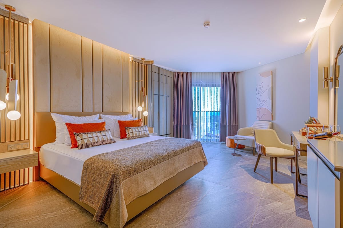 A modern hotel room with a large bed, a desk, and a view of the outdoors.