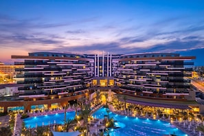 Un hotel moderno con piscina central, varios balcones y una fachada simétrica.