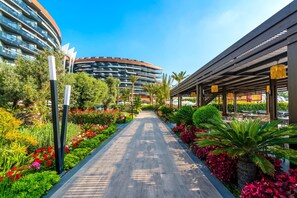 A pathway lined with vibrant flowers and greenery, leading to a modern building with a curved facade. - Calyptus Kirman Premium - Ultra All Inclusive (Manavgat)