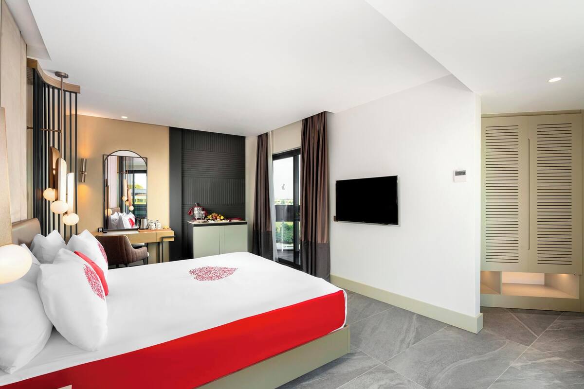 A modern hotel room with a large bed, a desk with a computer, a flat-screen TV, and a balcony with a view.
