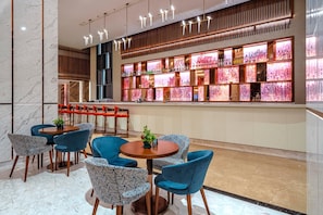 Un bar moderno con suelo de mármol, sillas azules, una mesa redonda y una pared con estanterías iluminadas.
