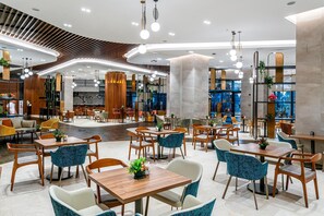A spacious indoor area with multiple seating arrangements, including tables and chairs, and a central open space. - Calyptus Kirman Premium - Ultra All Inclusive (Manavgat)