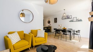 Una sala de estar moderna con dos sillones amarillos, un espejo redondo y un comedor con mesa y sillas.