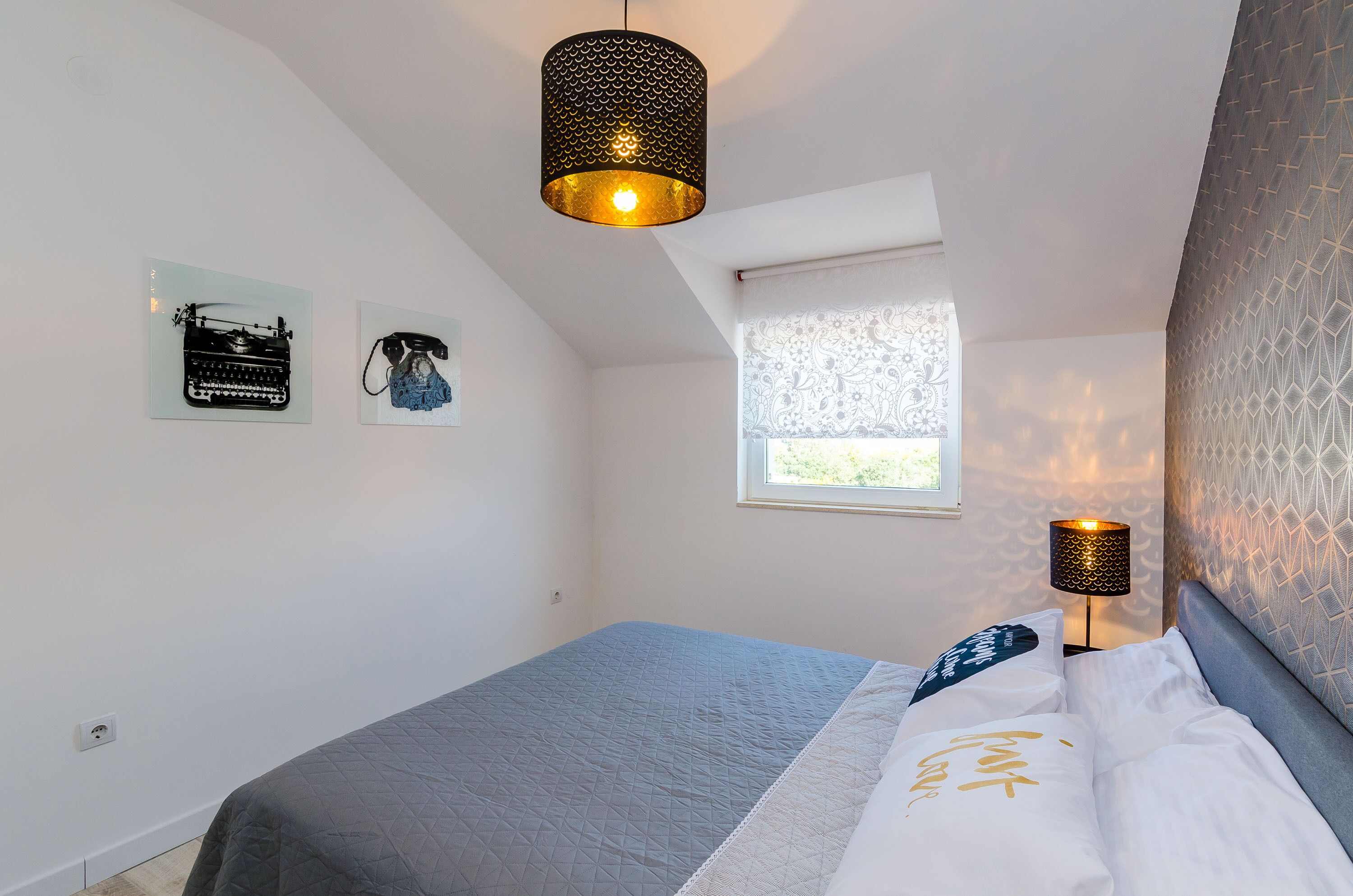 A bedroom with a bed, a window, and a hanging light fixture.