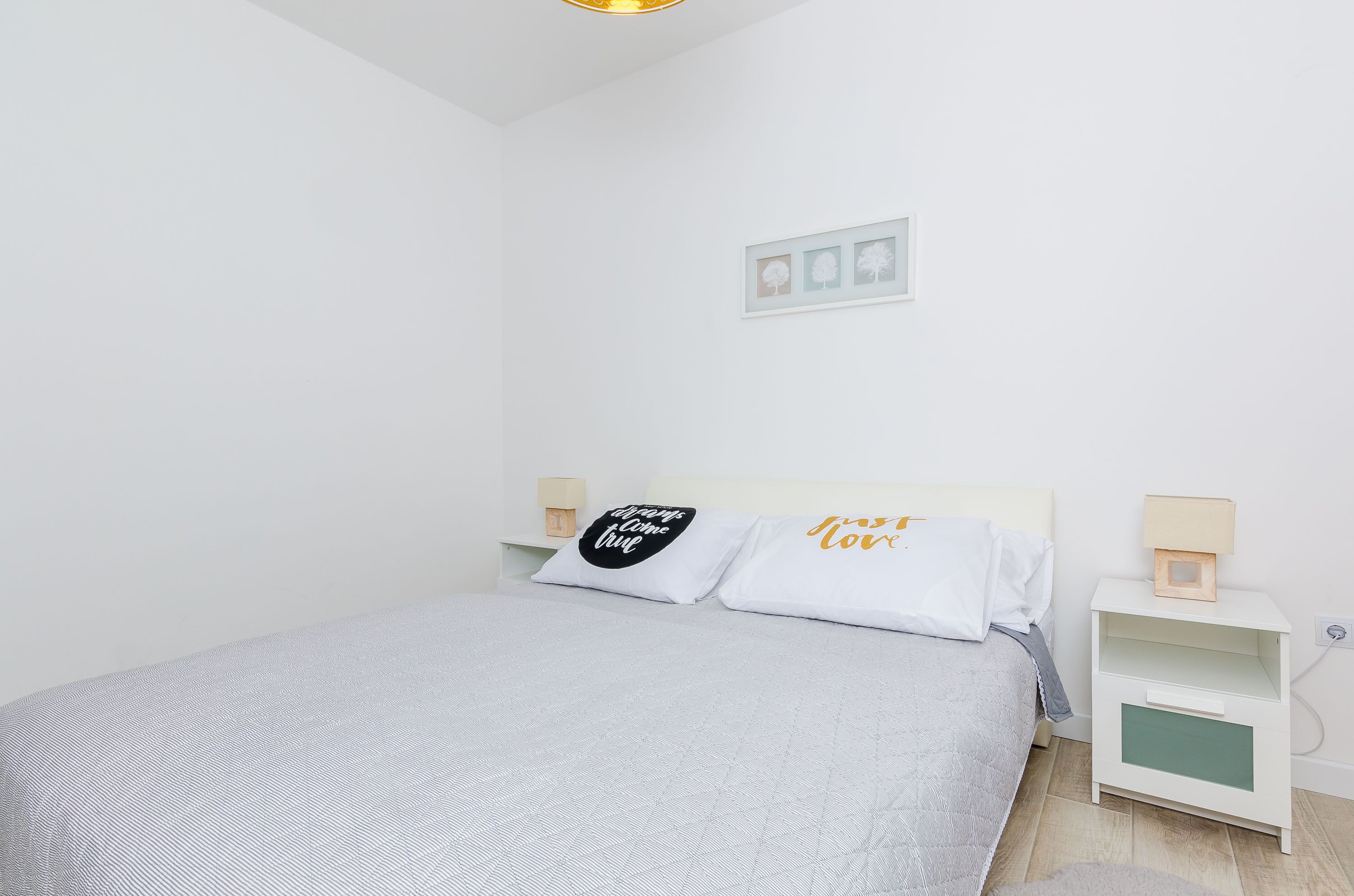 A neatly arranged bedroom with a bed, pillows, a nightstand, and a wall-mounted shelf.