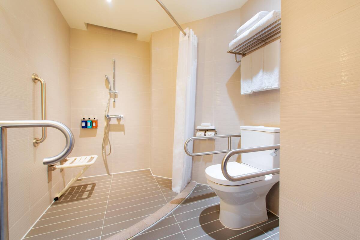 A bathroom with a shower, toilet, and grab bars.