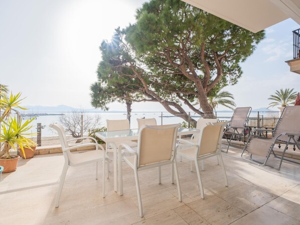 An outdoor patio with white furniture, a large tree, and a view of the sea.