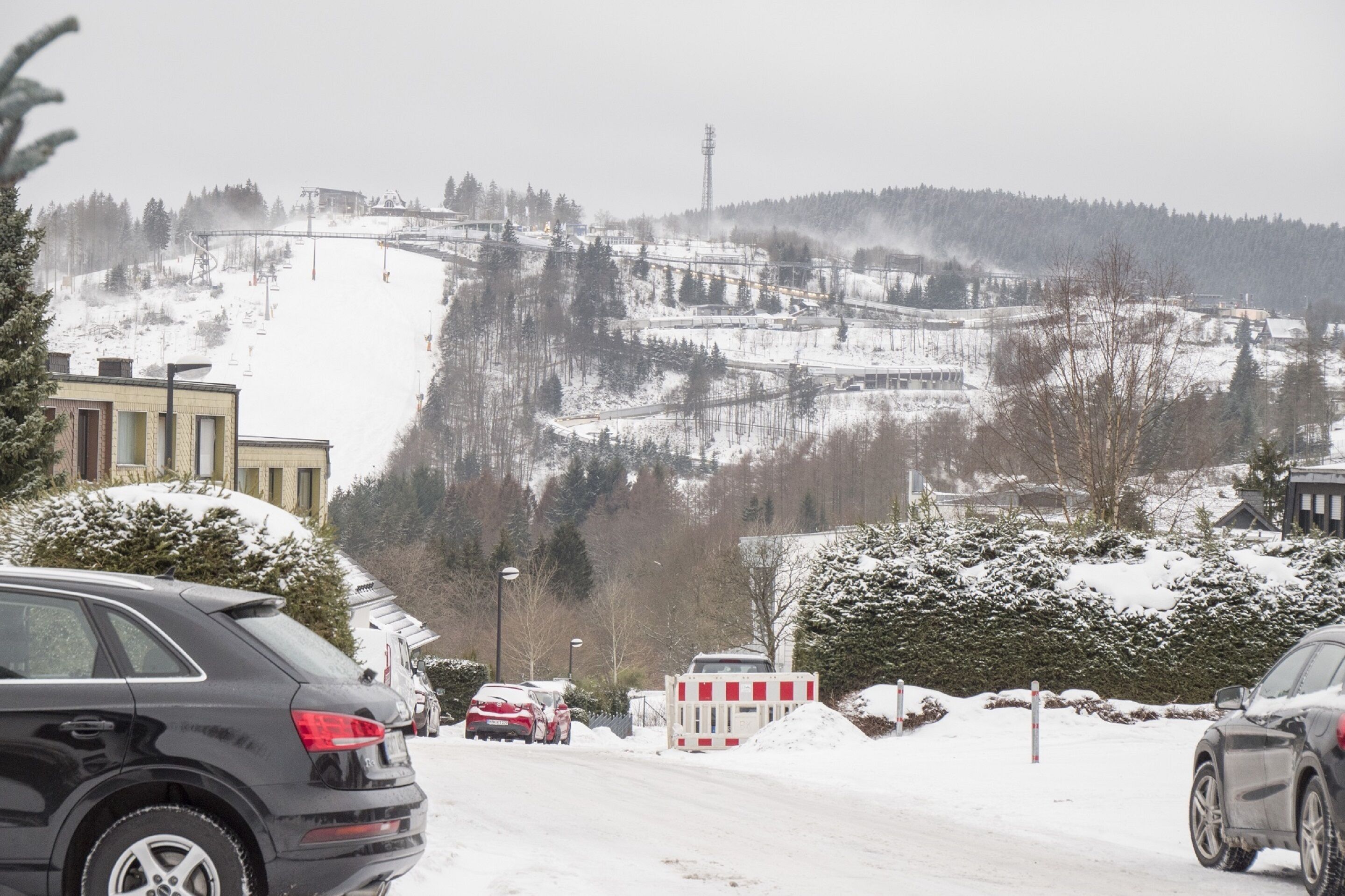 Paesaggio innevato con una seggiovia, edifici e auto parcheggiate.