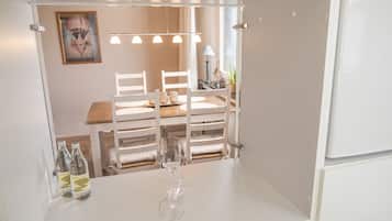 A compact room with a dining table and chairs, a small table with a glass and bottles, and a framed picture on the wall.