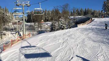 A ski lift with chairs moving along a snowy slope, surrounded by trees and a clear sky.