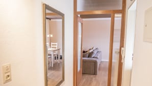 Un pasillo con un espejo, una puerta que da a una sala de estar con un sofá y una mesa.