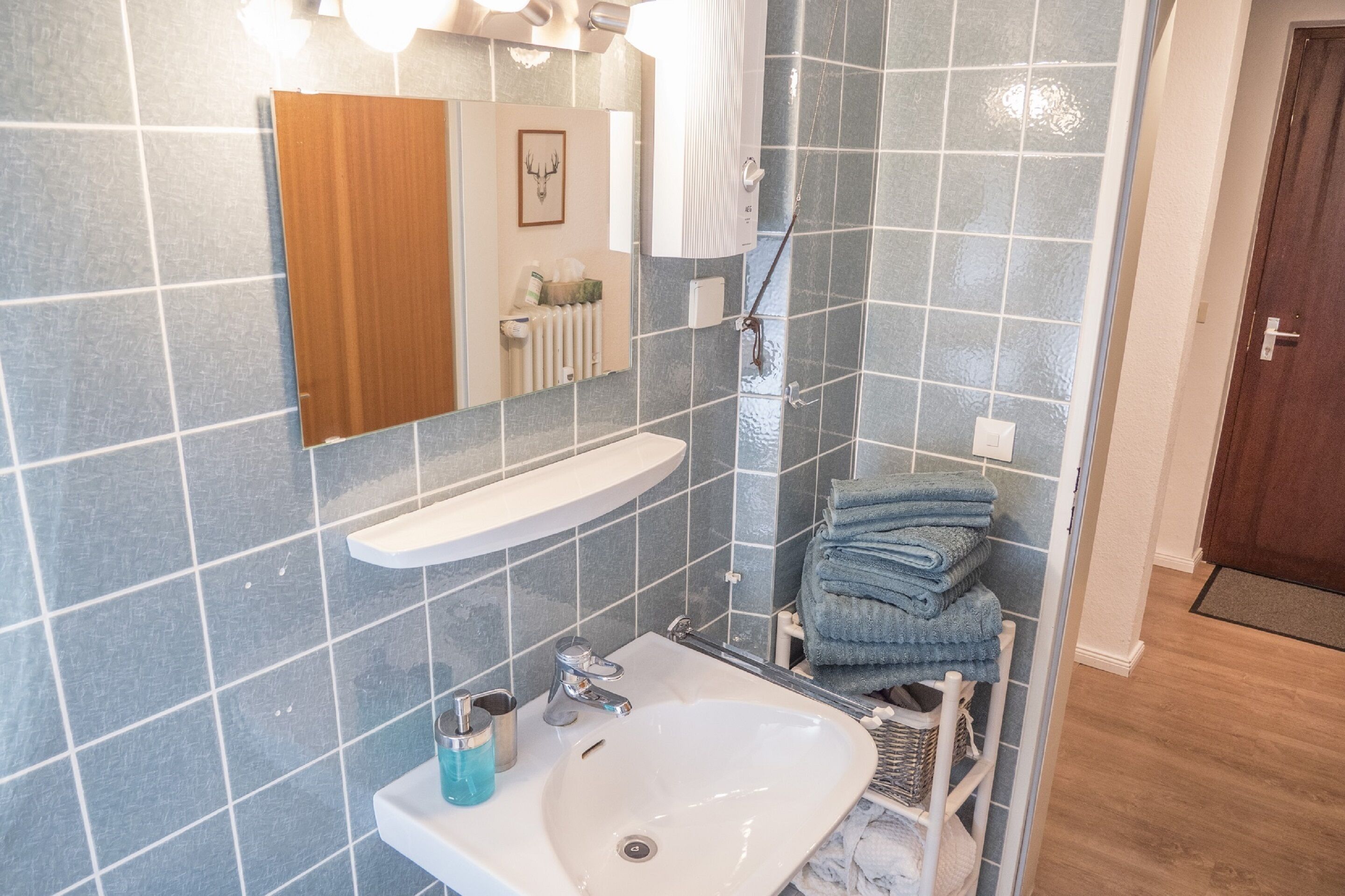 A bathroom with a white sink, a mirror, a towel rack with folded towels, and a shower area.