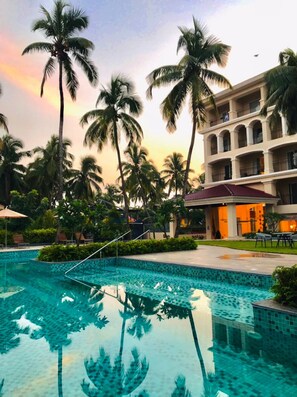 A swimming pool with palm trees and a building with balconies. - Holiday Inn Goa Candolim by IHG (Candolim)