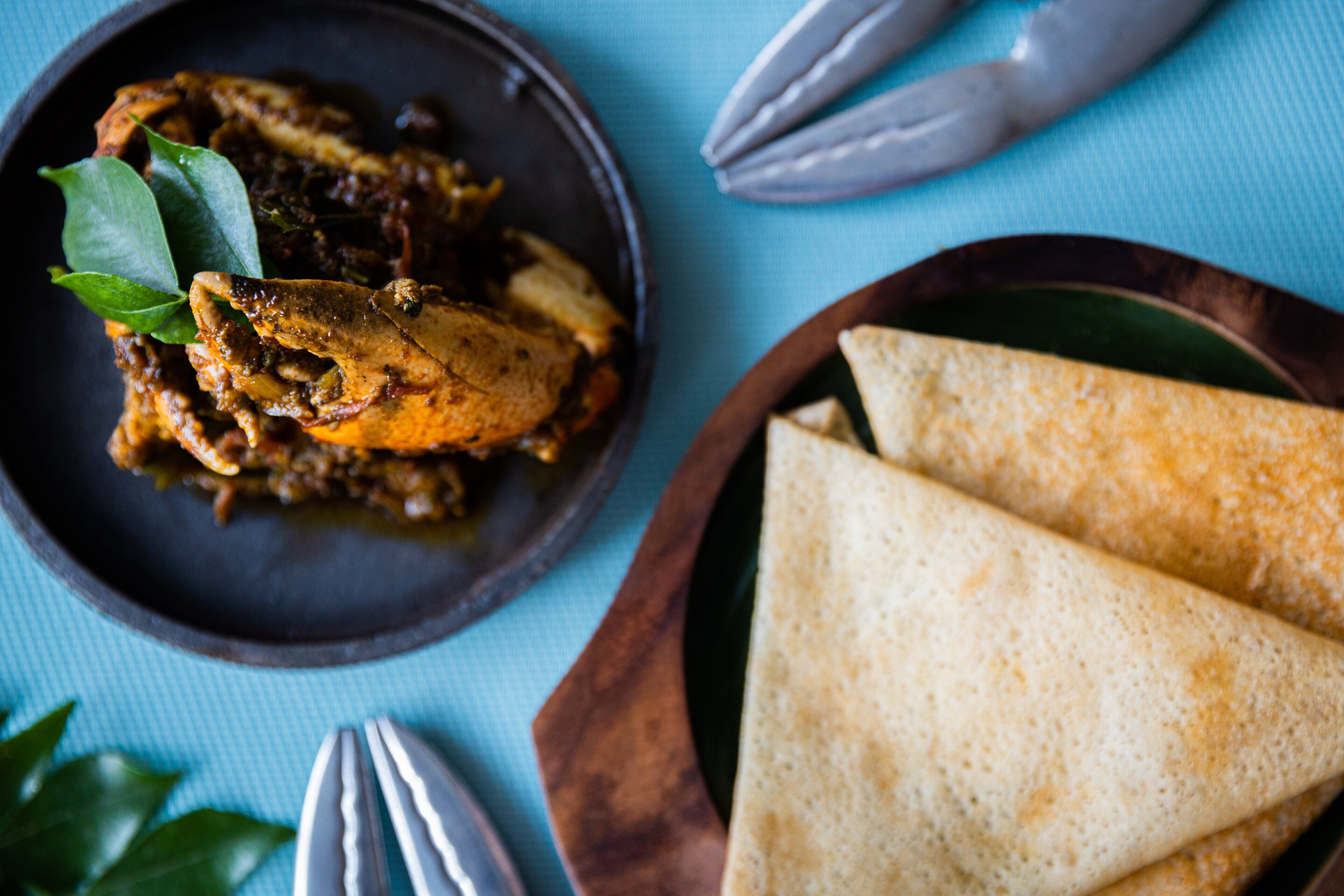 A plate of food with a bowl of curry and two folded flatbreads on a wooden board.