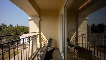 A balcony with two chairs and a table, a glass door, and a view of greenery.