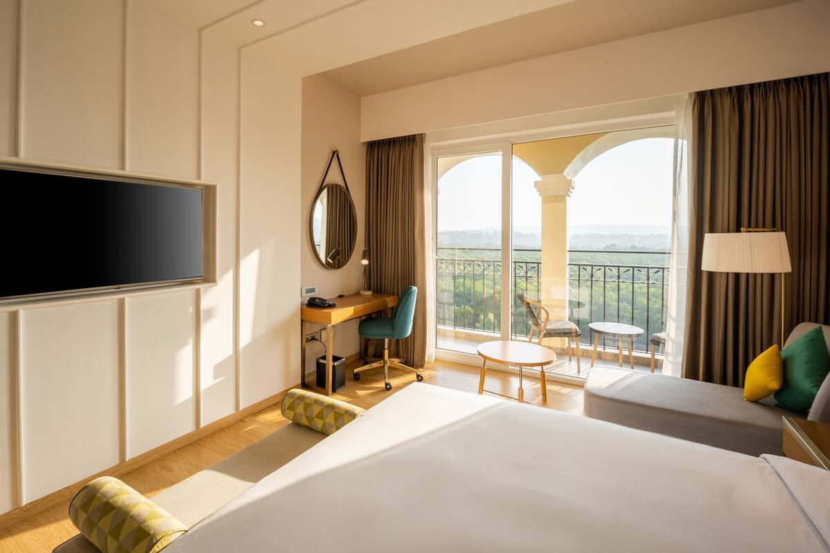 A hotel room with a bed, a desk, a chair, a TV, and a balcony with a view.