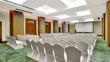 A conference room with rows of white chairs, a projector screen, and a green patterned carpet.