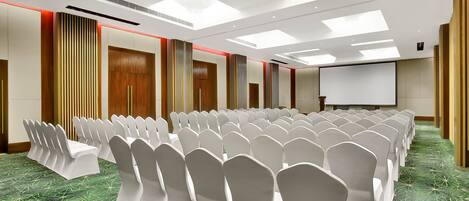 A conference room with rows of white chairs, a projector screen, and a green patterned carpet.