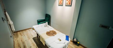 A room with a wooden floor, a bed with a white bedspread, a green chair, and two framed pictures on the wall.