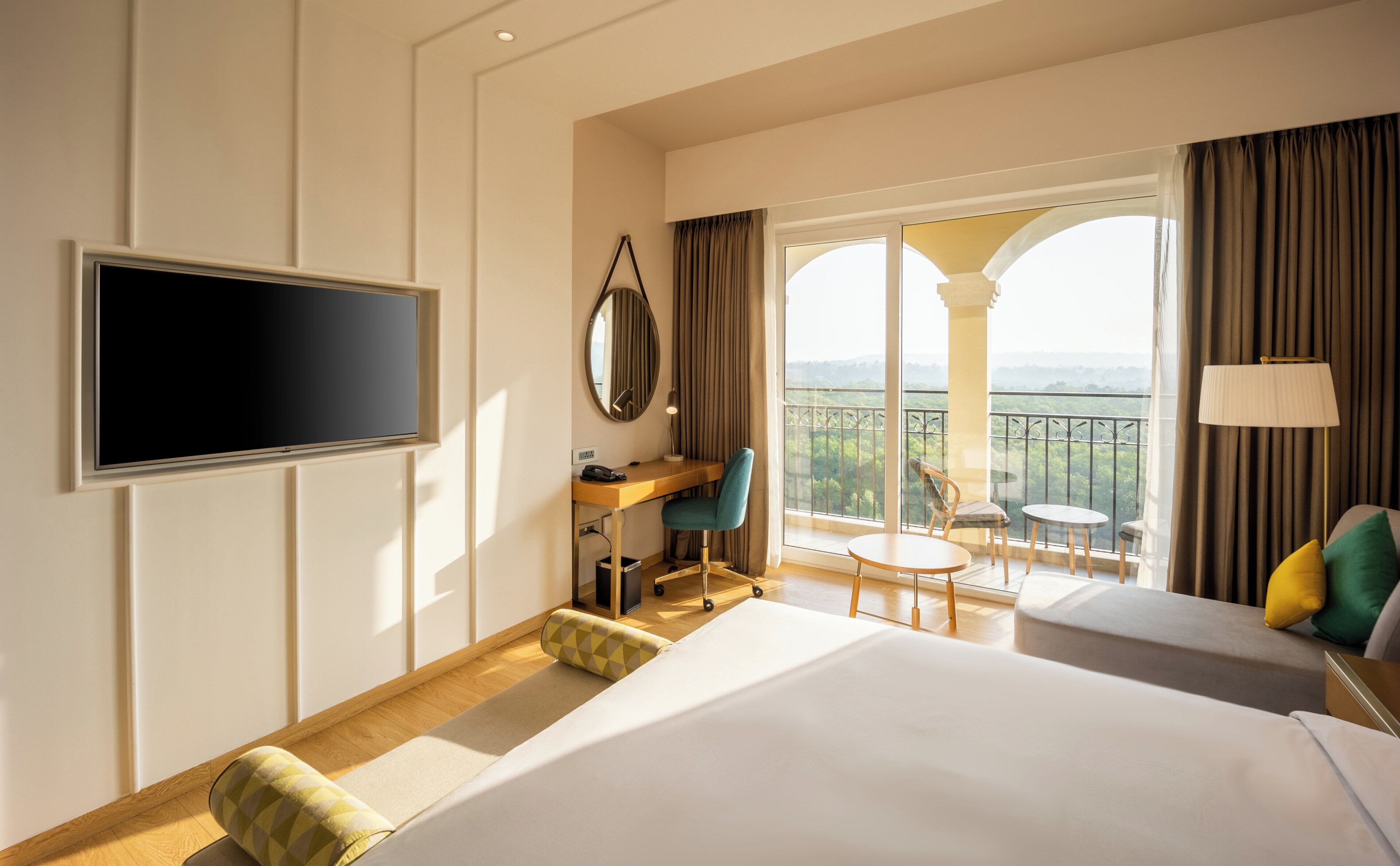 Habitación de hotel con cama, escritorio, silla, televisión y balcón con vistas.