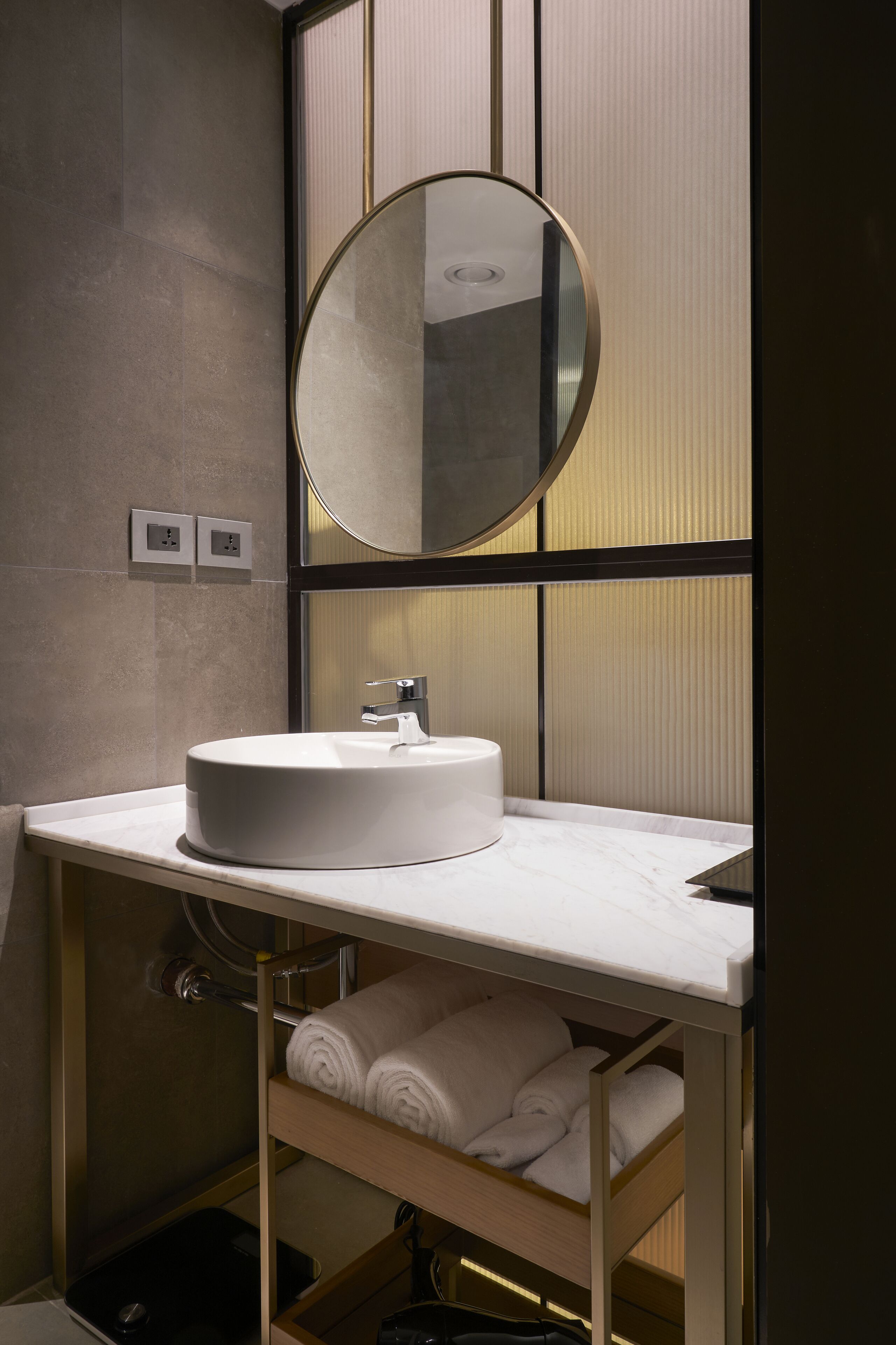 Een moderne badkamer met een ronde spiegel, een witte wastafel en een handdoekhouder.