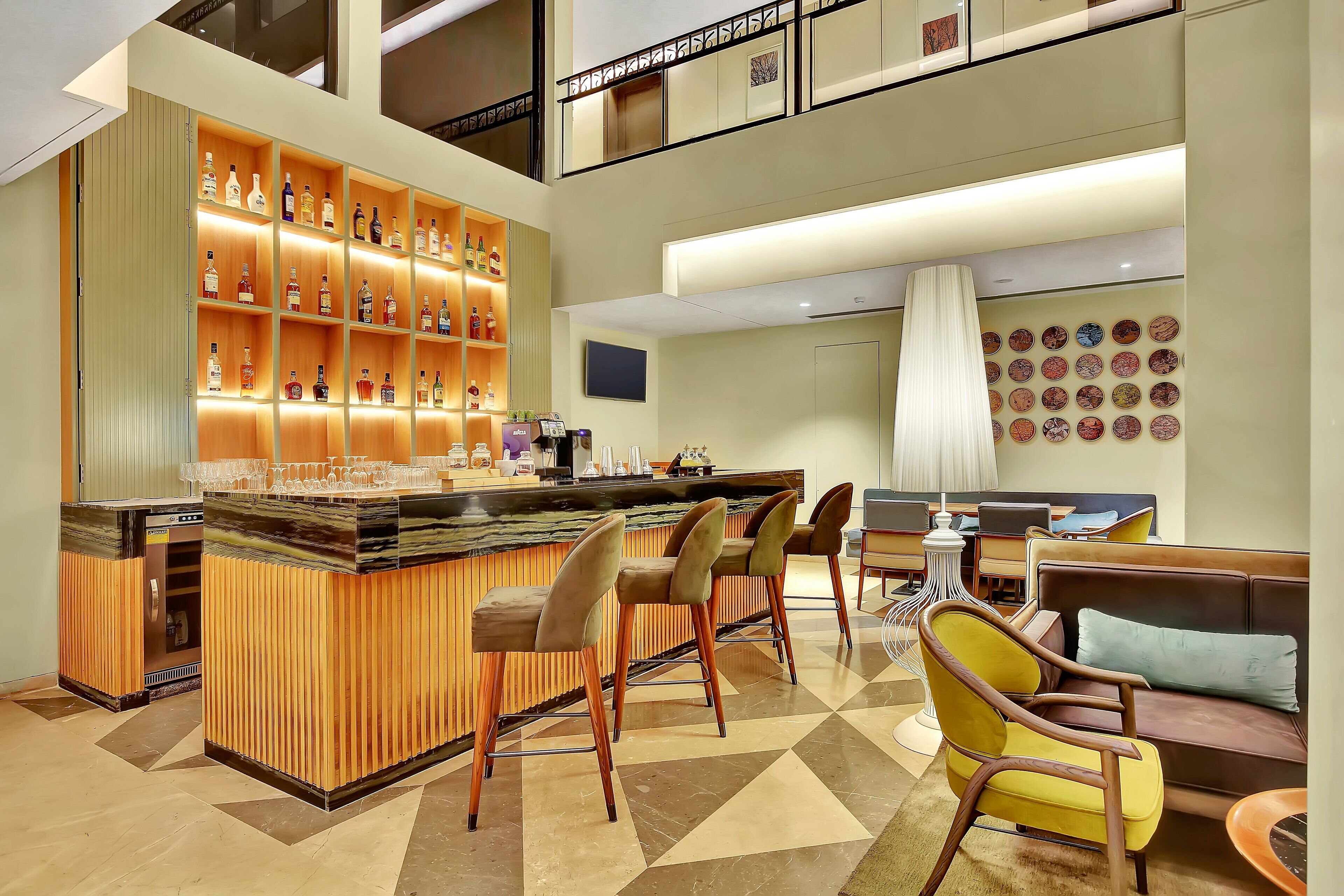 A bar area with a wooden bar counter, multiple stools, and a variety of bottles on shelves.