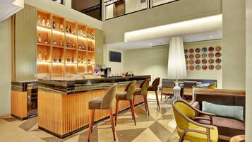 A bar area with a wooden bar counter, multiple stools, and a variety of bottles on shelves.