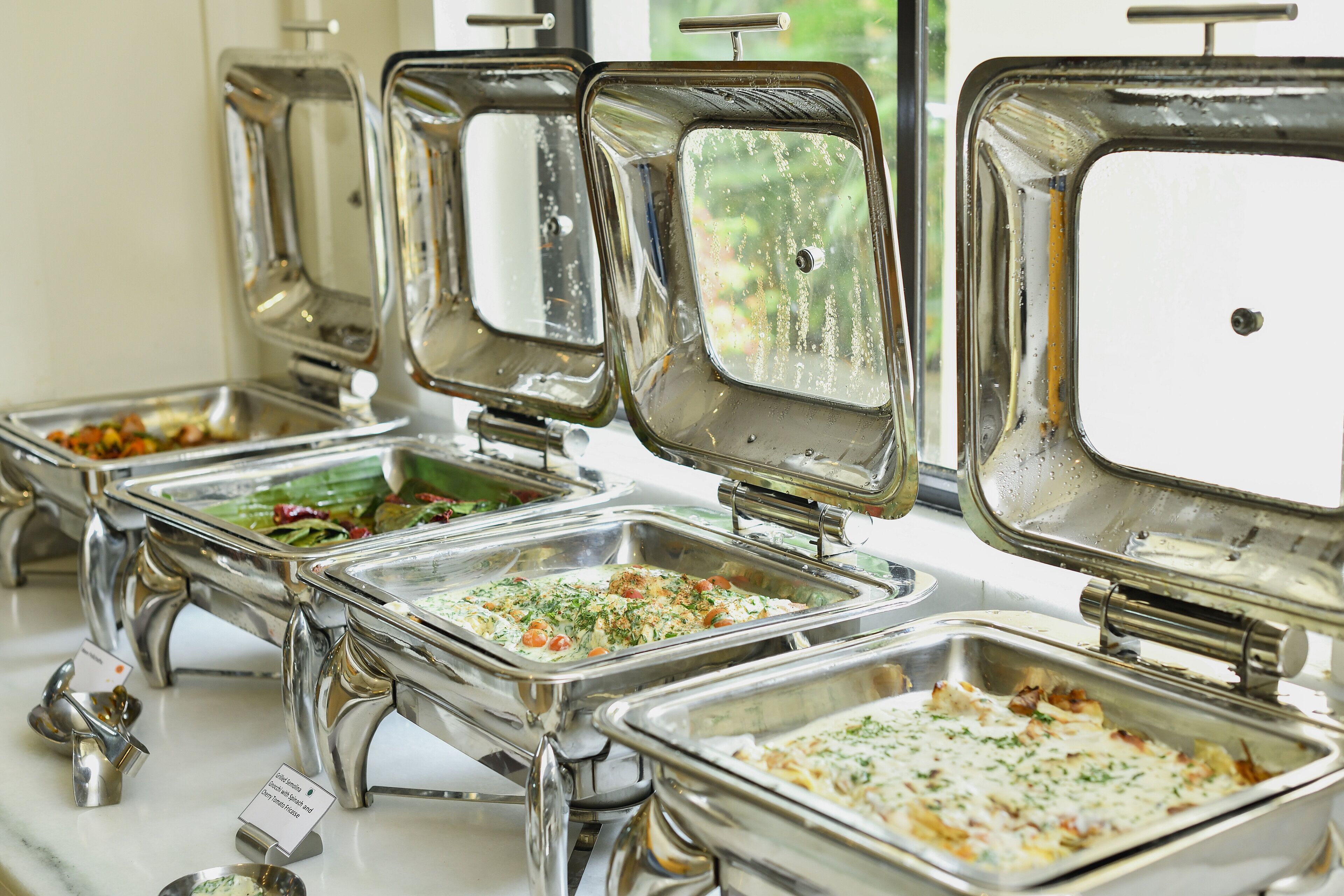 A buffet with multiple stainless steel serving trays, each containing different dishes.