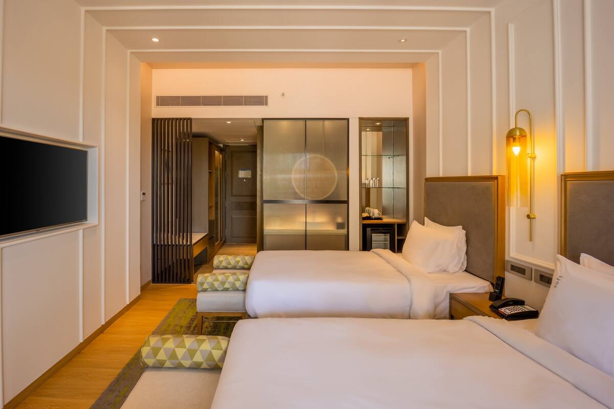 A hotel room with two beds, a television, a desk with a chair, and a wardrobe.