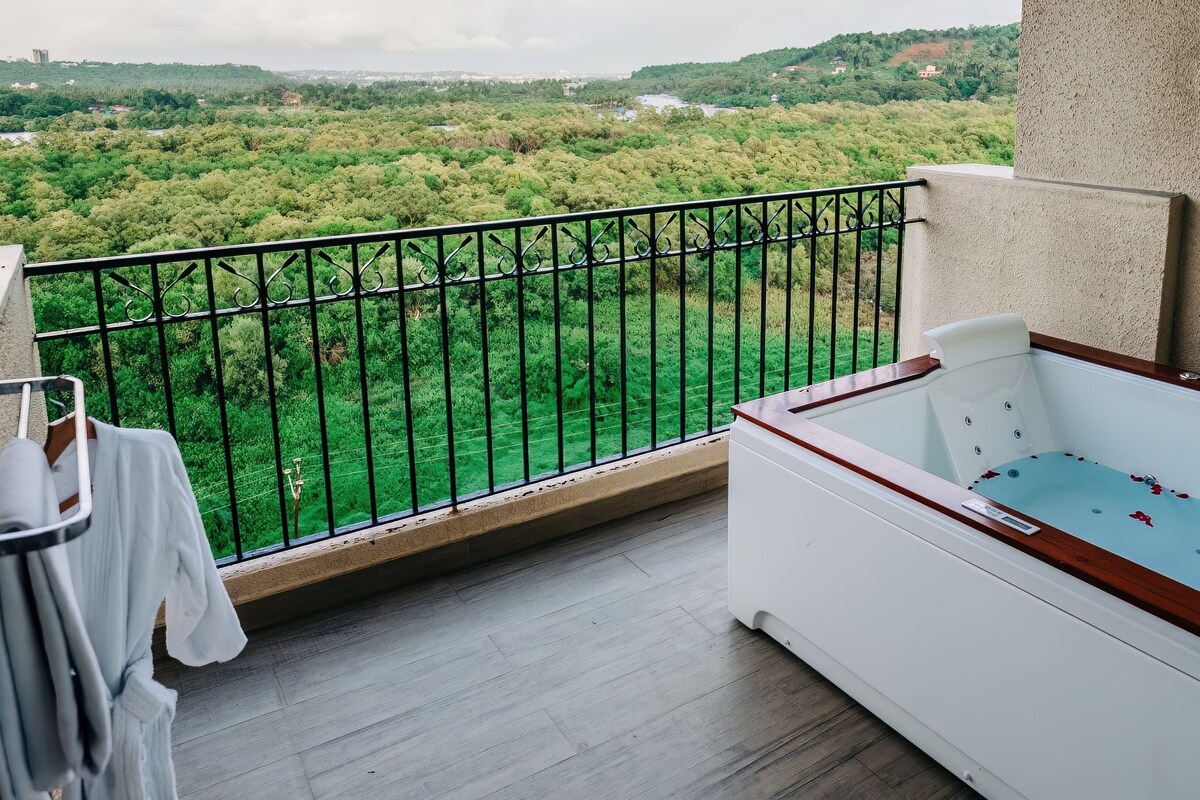 A balcony with a view of a lush green landscape, a white bathtub, and a towel rack with folded towels.