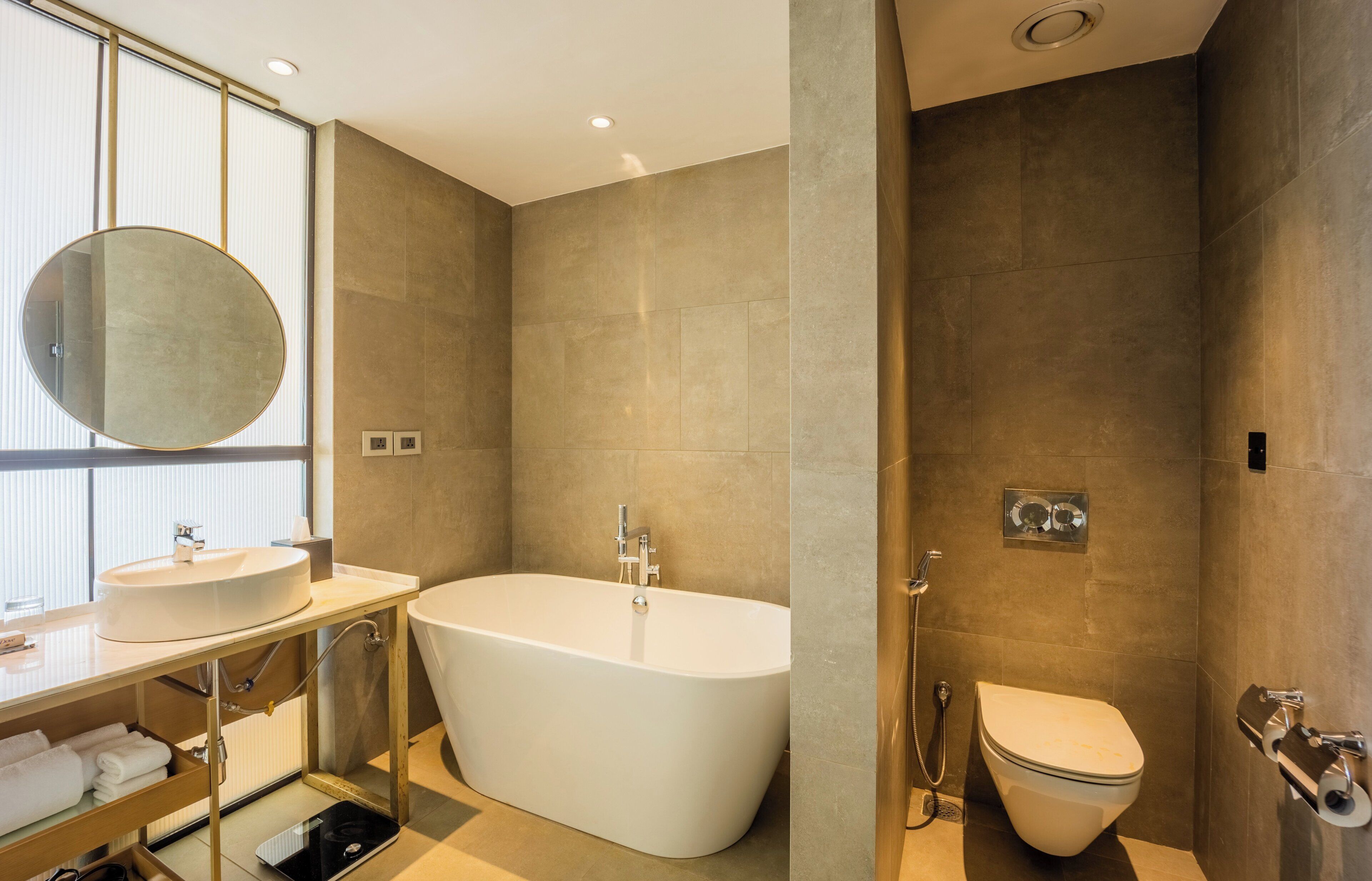 A modern bathroom with a freestanding bathtub, a round mirror, and a toilet.