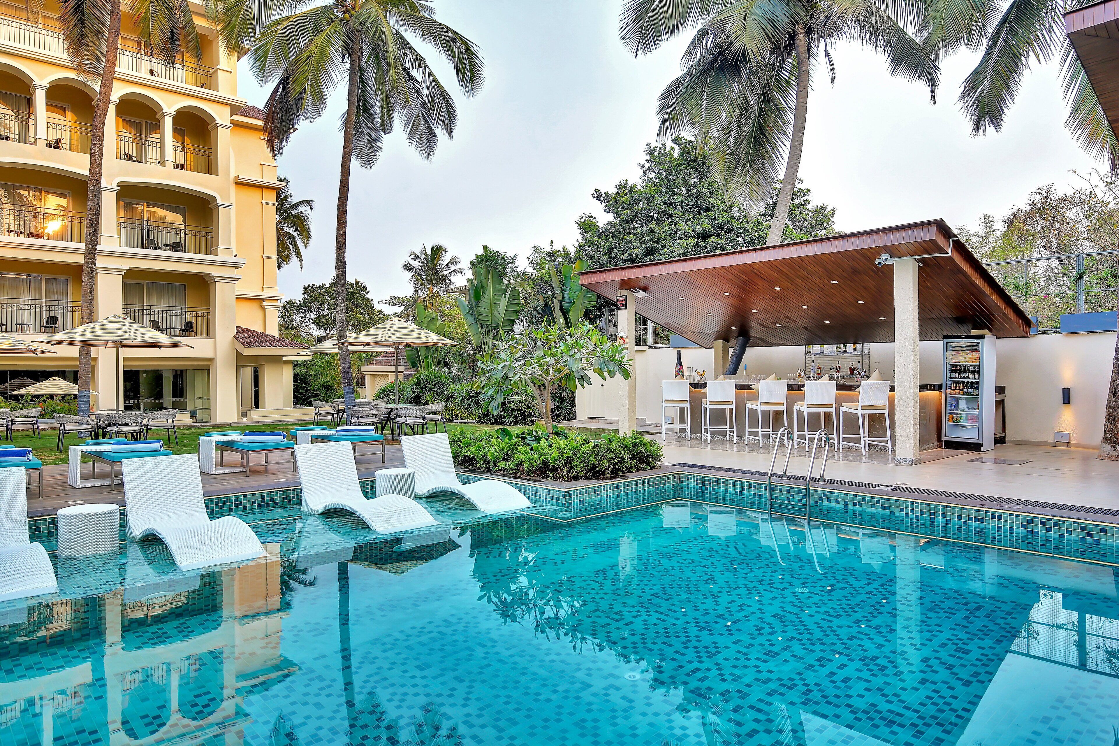 A hotel with a swimming pool, lounge chairs, and a covered bar area.