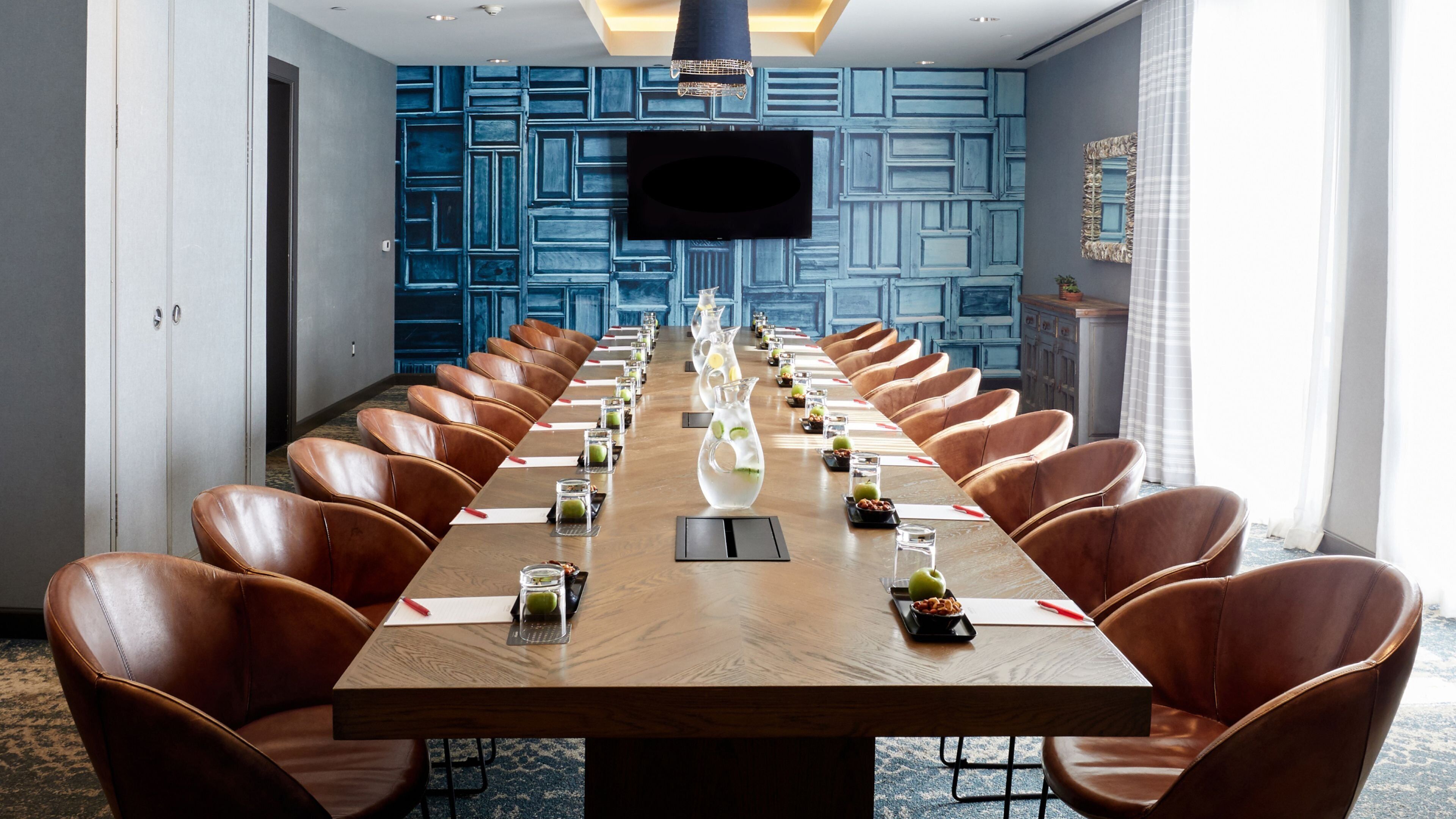 A conference room with a long table, brown leather chairs, and a flat-screen TV mounted on the wall.