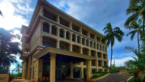 Um hotel com vários andares, entrada com piso de tijolos e palmeiras.