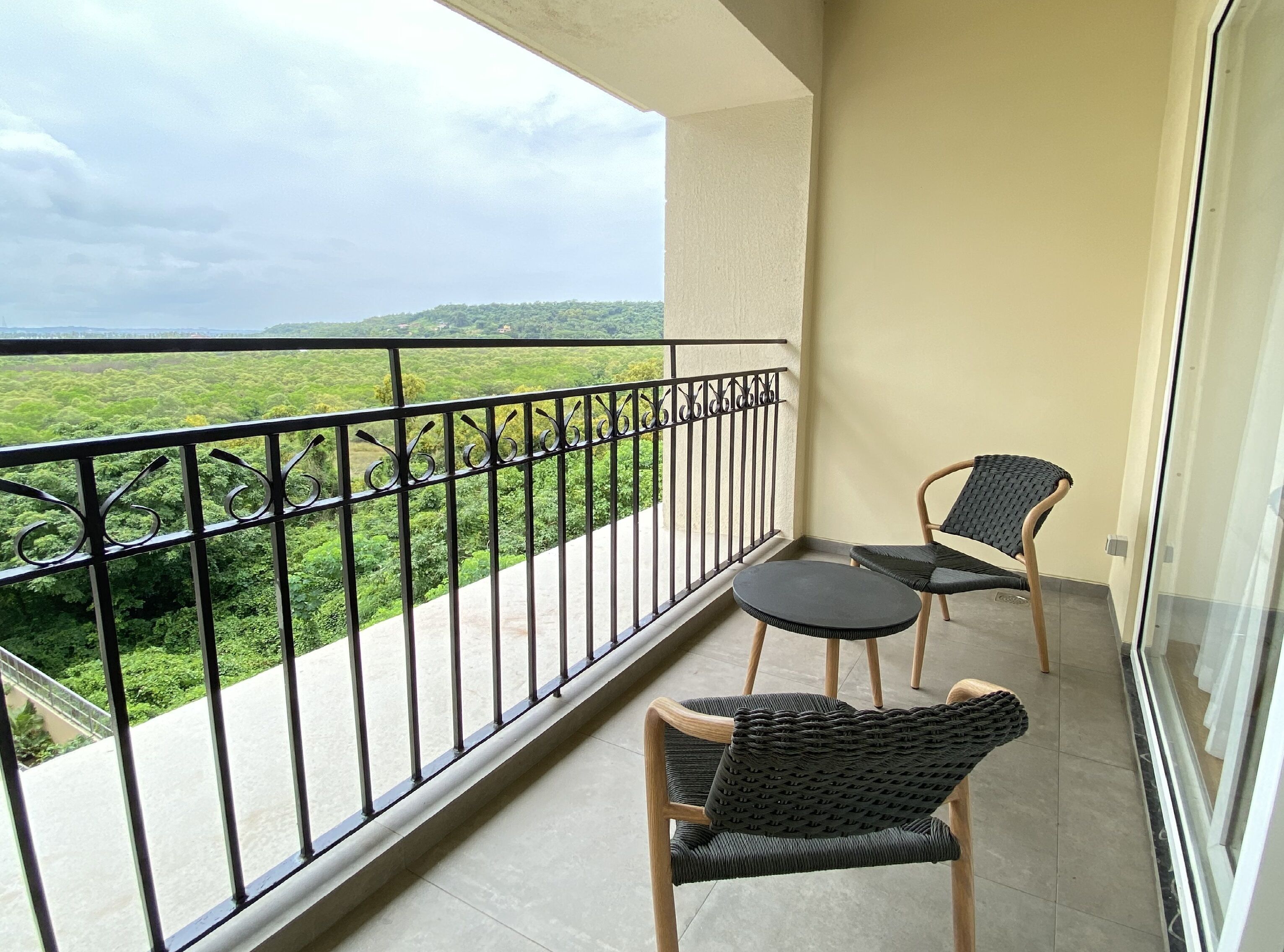 A balcony with a view of a green landscape, two wicker chairs, and a small round table.