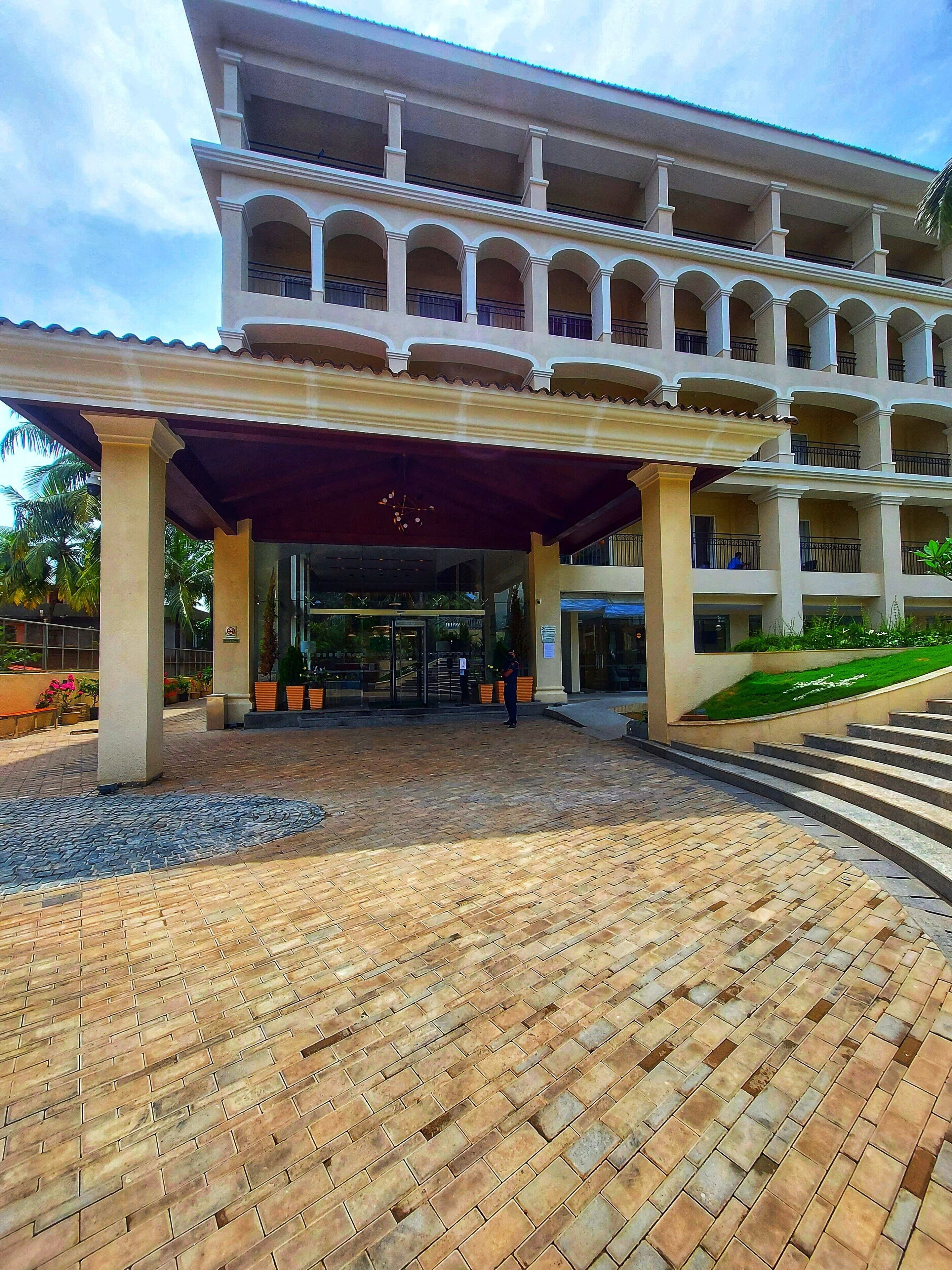 A hotel entrance with a covered walkway, multiple balconies, and a landscaped area with palm trees.