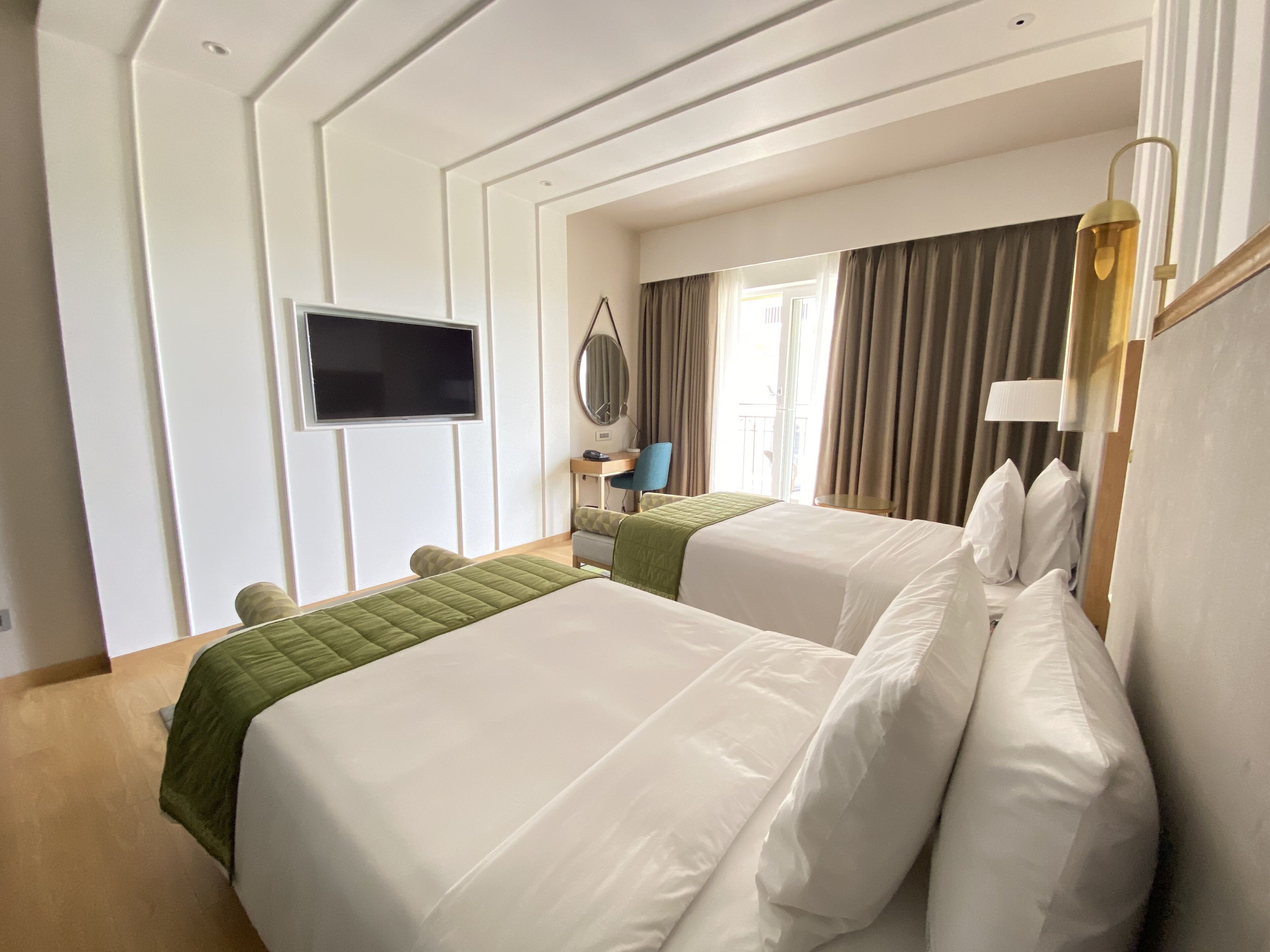 A hotel room with two beds, a TV, a desk, and a window with curtains.