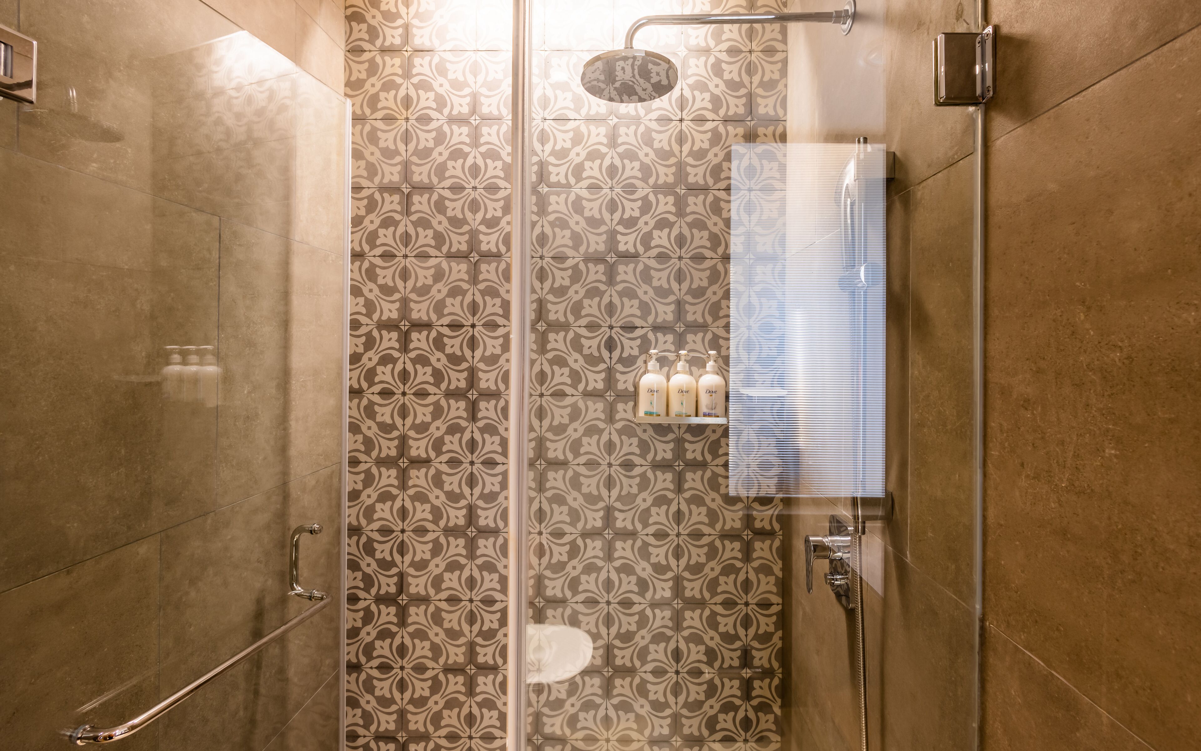 A shower with a glass door, patterned tiles, and a shelf with toiletries.