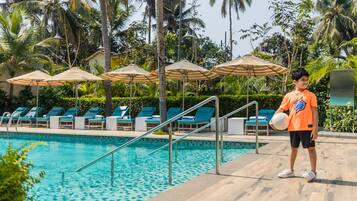 A poolside area with lounge chairs and umbrellas, surrounded by palm trees.