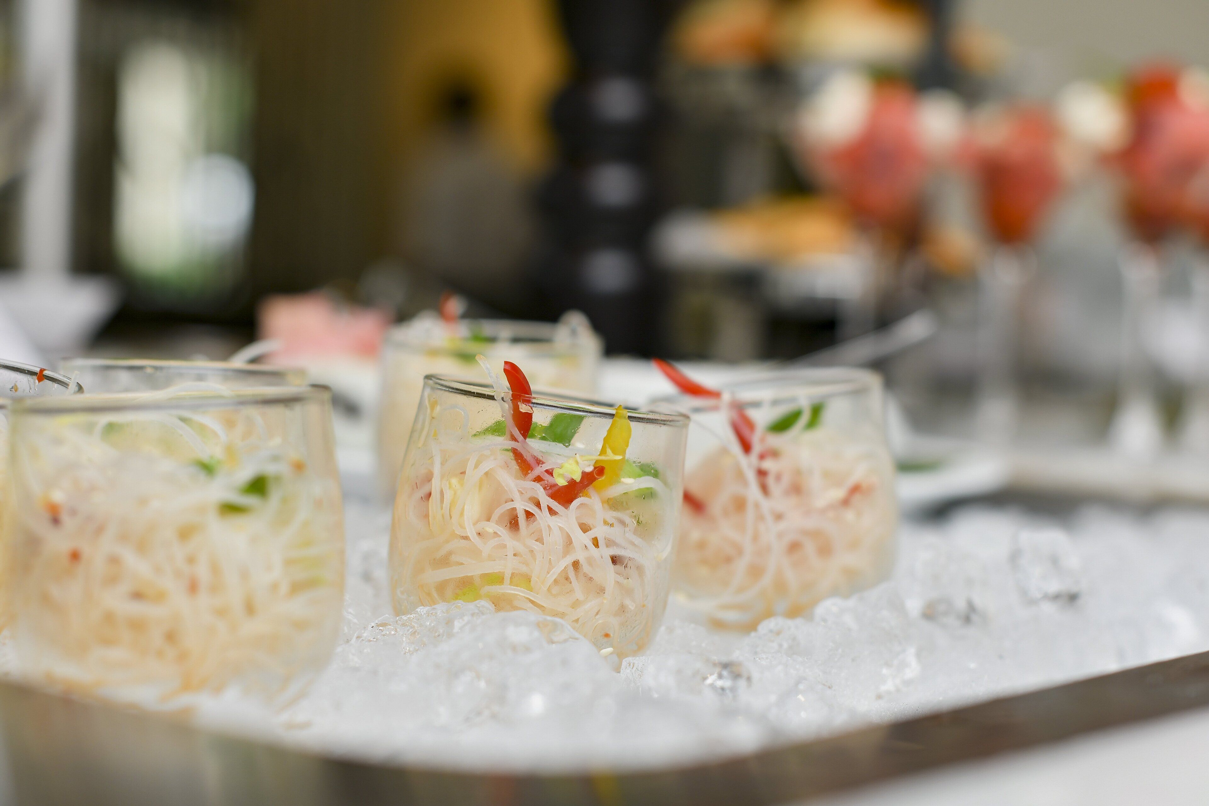 A tray of drinks with ice, containing a mixture of noodles and vegetables, garnished with red and green elements.