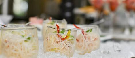 A tray of drinks with ice, containing a mixture of noodles and vegetables, garnished with red and green elements.